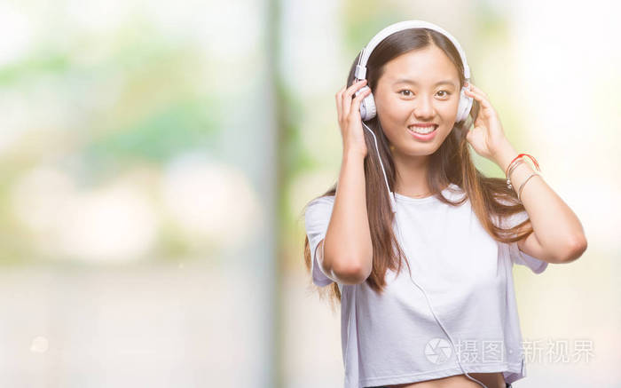 年轻的亚洲女人听音乐,戴着耳机,背景与快乐的脸站着