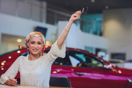 美丽的女人享受快乐的时刻得到汽车钥匙从汽车销售商汽车沙龙。穆斯林妇女在头巾