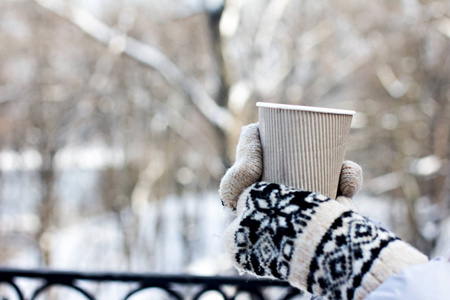 s hands in mittens hold a craft paper glass