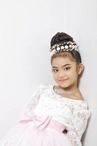 亚洲可爱的年轻女孩戴着皇冠和一件白色连衣裙，在白色的墙壁背景上度假时带着可爱的微笑。