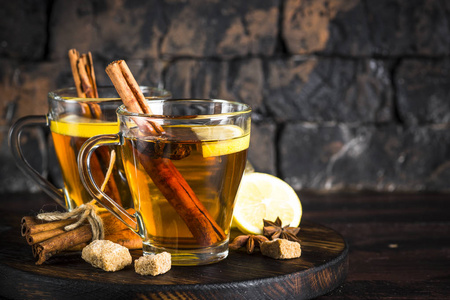 秋季热茶与柠檬和香料在玻璃杯在黑暗的背景。