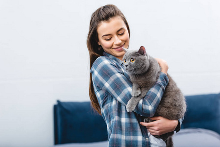 微笑的年轻女子抱着可爱的英国短毛猫