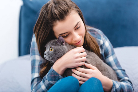 在卧室里拥抱可爱的英国短毛猫的女孩