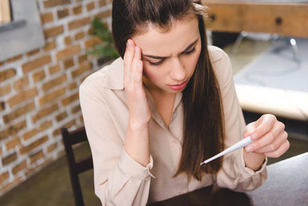 生病的年轻女商人拿着温度计在办公室检查温度