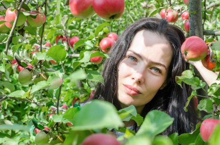 美丽的黑发女孩肖像背景苹果树枝与大红苹果。 夏日的心情。 摘苹果。 丰收。 伊娃风格