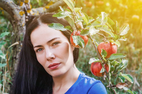 的黑发女孩在一个野生花园附近的一棵苹果树的树枝上有一个大红苹果。 靠大自然休息。 妇女健康。 夏天的记忆。 性女性