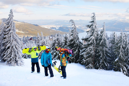 三个滑雪者在滑雪场散步。朋友们带着滑雪板爬到山顶, 穿过森林, 穿着反光护目镜, 穿着五颜六色的时尚服装