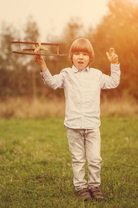 儿童飞行员与飞机在日落小男孩玩纸板玩具飞机户外夏季天空背景。 复古色调。 梦想旅行