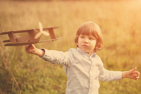 儿童飞行员与飞机在日落小男孩玩纸板玩具飞机户外夏季天空背景。 复古色调。 梦想旅行
