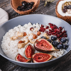 大米椰子粥与无花果浆果，坚果，干燥杏和椰子牛奶在盘子上的乡村木制背景。 健康的早餐配料。 清洁吃纯素食品的概念。 顶部视图
