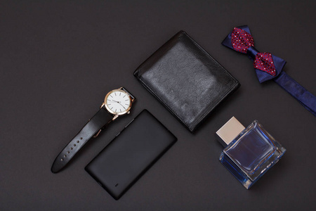 皮革钱包手表与黑色皮革皮带古龙水男子蝴蝶结领带和手机在黑色背景。 男人的配饰。 上面的风景。