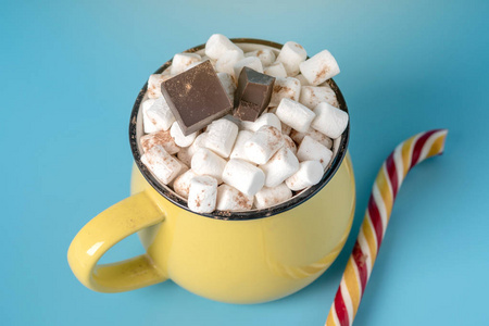 一杯热巧克力，上面有棉花糖，在蓝色背景上贴上棒棒糖。 舒适温暖的冬卡