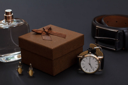 古龙水为男性棕色礼品盒袖扣手表与黑色皮带和皮带与金属扣在黑色背景。 男人的配饰。