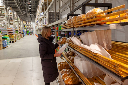 一个穿着长夹克的金发女孩在面包店购物时选择食物，在大量的货架和柜台中购物