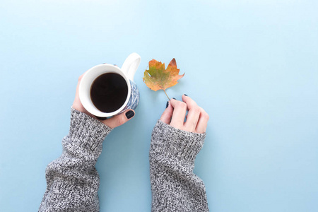 手拿着一杯刚冲泡的黑色咖啡，秋天的叶子平躺在蓝色的背景上。