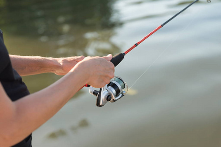 s hands are fishing on a spinning in the water on a sunny summer