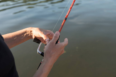 s hands hold a  spinning over the water while fishing.