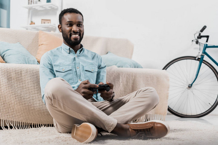 非裔美国人坐在地板上，两腿交叉，玩电子游戏