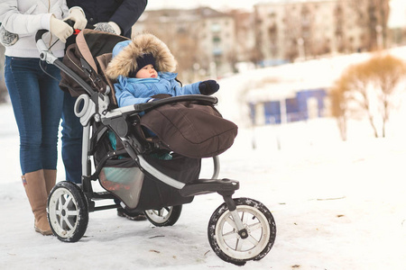 快乐的年轻家庭走在冬季公园, 妈妈, 爸爸和儿子在婴儿车