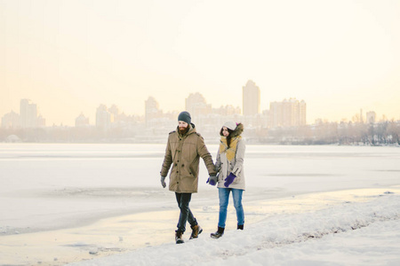 主题圣诞假期冬季新年。 年轻时尚的高加索爱情夫妇在冰冻的湖岸上进行无性行走。 日期。 情人节在冬天的日落。 爱情和浪漫的主题。