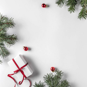 创意框架由圣诞杉枝在白纸背景上与红色装饰松果。 圣诞节和新年主题。 平躺式顶部视图