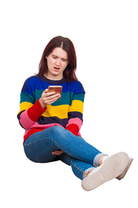 沮丧的年轻女子坐在地板上浏览智能手机，消极的脸，情感，震惊的表情，孤立的白色背景。