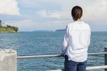 年轻的亚洲女士在桥的后面看着大海。