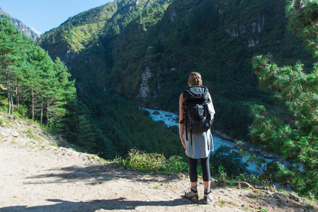 美丽的场景，年轻的徒步女站在美丽的山和瀑布前面，她的背包和徒步杆。