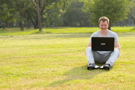 年轻快乐的男人坐在公园里用笔记本电脑