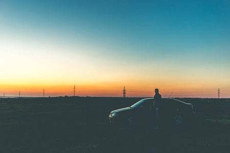 日落时一个年轻人和一辆黑色的车。