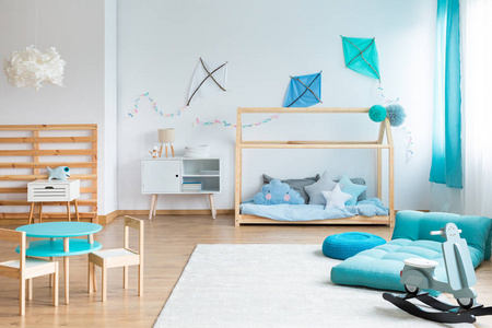 在斯堪的纳维亚婴儿卧室的空白墙上放着DIY蓝色风筝，带蒲团，带枕头的房子形状的床