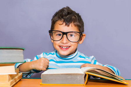 快乐的男孩带着眼镜在书房的桌子上拿着书