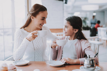 夫妇正在咖啡馆里休息。 夫妻是一对美丽的年轻母女。 人们从杯子里喝茶。 人们坐在桌子旁。 人们互相看着，微笑着。