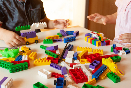 合上孩子们的手在桌子上玩彩色塑料砖。 蹒跚学步的孩子玩得开心，用明亮的建筑砖建造。 早期学习。