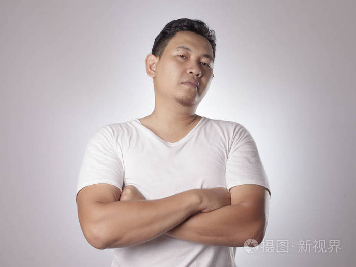 的亚洲男人的肖像穿着休闲的白色衬衫,微笑着,露出骄傲的手势交叉手臂