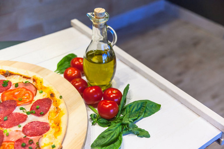 白桌上有香肠火腿橄榄油和罗勒的开胃披萨