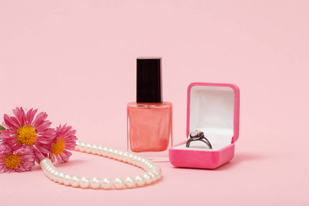 戒指在盒子里，指甲油珠在粉红色背景的绳子上。 女性珠宝化妆品和配件。
