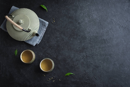 茶壶和茶杯在黑色背景复制空间。 传统的亚洲茶具，铁茶壶和陶瓷茶杯，绿茶和茶叶。