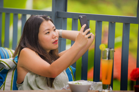 年轻快乐迷人的亚洲女性户外咖啡厅，喝果汁，自拍，用手机自拍，热带岛屿，摆姿势，放松，享受假期，旅行
