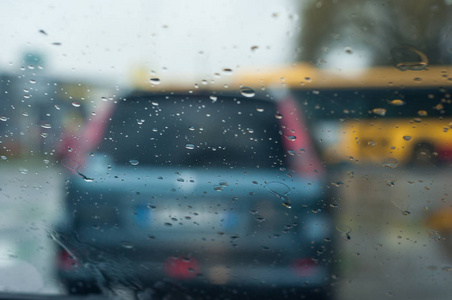 雨滴在挡风玻璃上的特写，背景上模糊的汽车