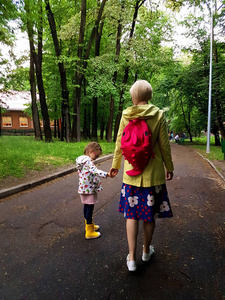 母亲和小孩卷发女孩一起在公园散步后雨，夏季多雨日视图从后面