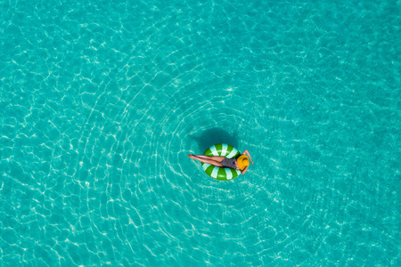在塞舌尔透明的绿松石海中游泳圈上游泳的苗条女人的空中景色。夏日海景带少女，美丽海浪，缤纷水色..无人驾驶飞机的俯视图