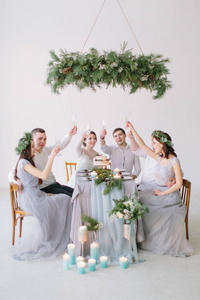 一群人坐在装饰着松树鲜花和蜡烛的白色大厅的婚礼桌旁