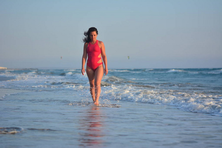 漂亮快乐的黑发女孩穿着红色泳衣在海滩上摆姿势。