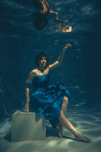 优雅漂亮的女人在水下游泳，就像一个独自穿着蓝色晚礼服的自由潜水员