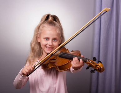 微笑的小女孩，穿着优雅的衣服，拉着小提琴，靠近