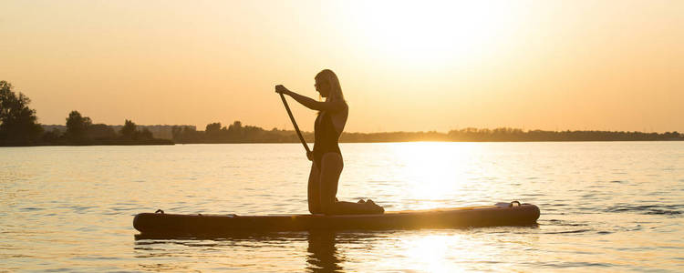 年轻的女人游泳站起来划桨板。水上运动积极的生活方式。
