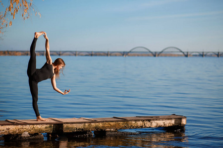 年轻女子在安静的木制码头练习瑜伽，有城市背景。 城市高峰中的运动和娱乐。