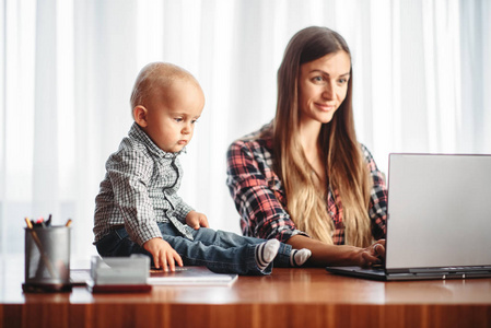 妈妈和小孩看着笔记本电脑屏幕。 妈妈和儿子在家一起快乐