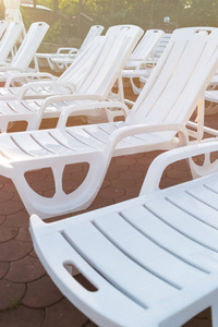 日落时海滩上石砖铺上的白色塑料躺椅。 日落放松假期假期概念